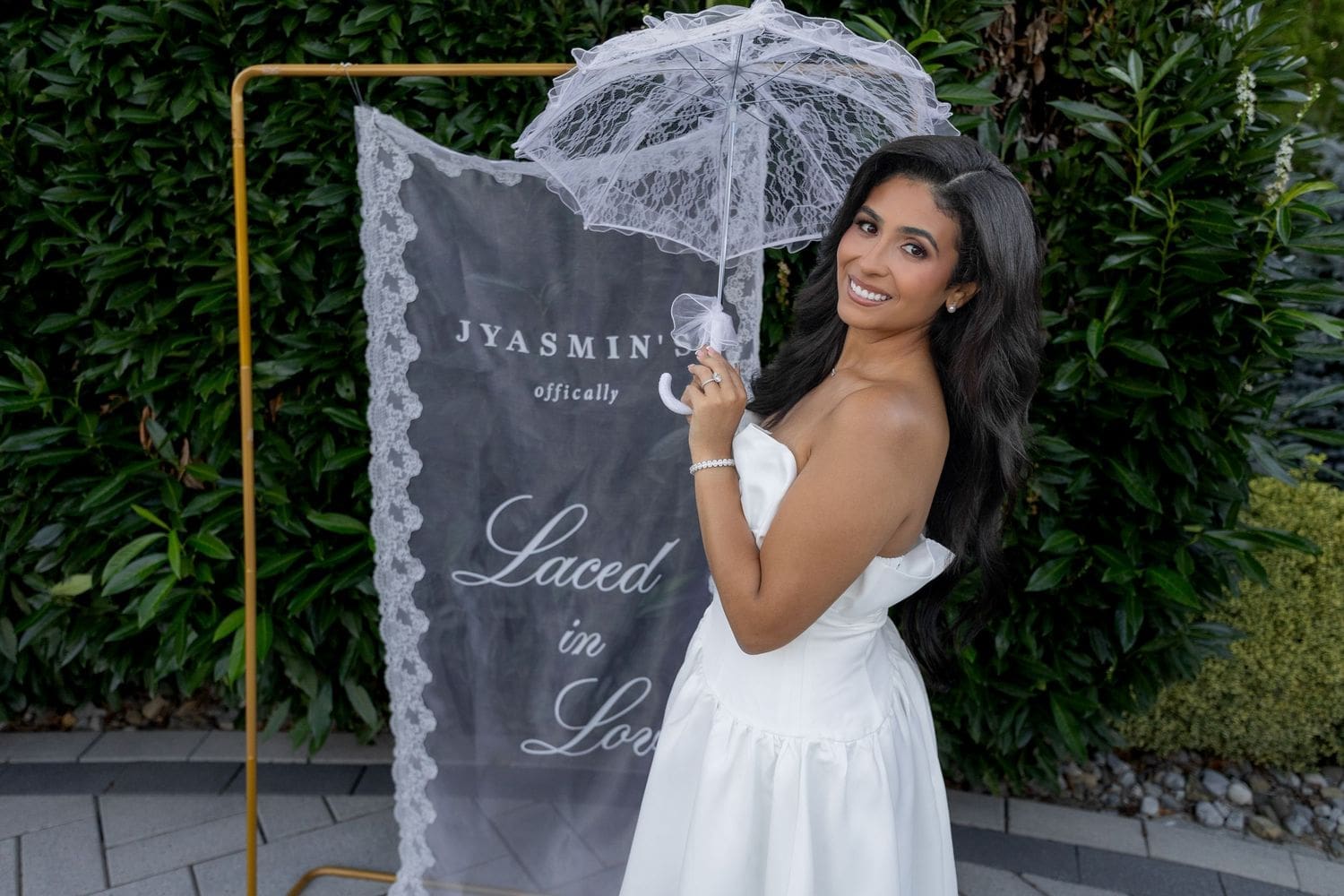 Bride-to-be with a lace parasol beside her Laced in Love sign at her backyard bridal shower