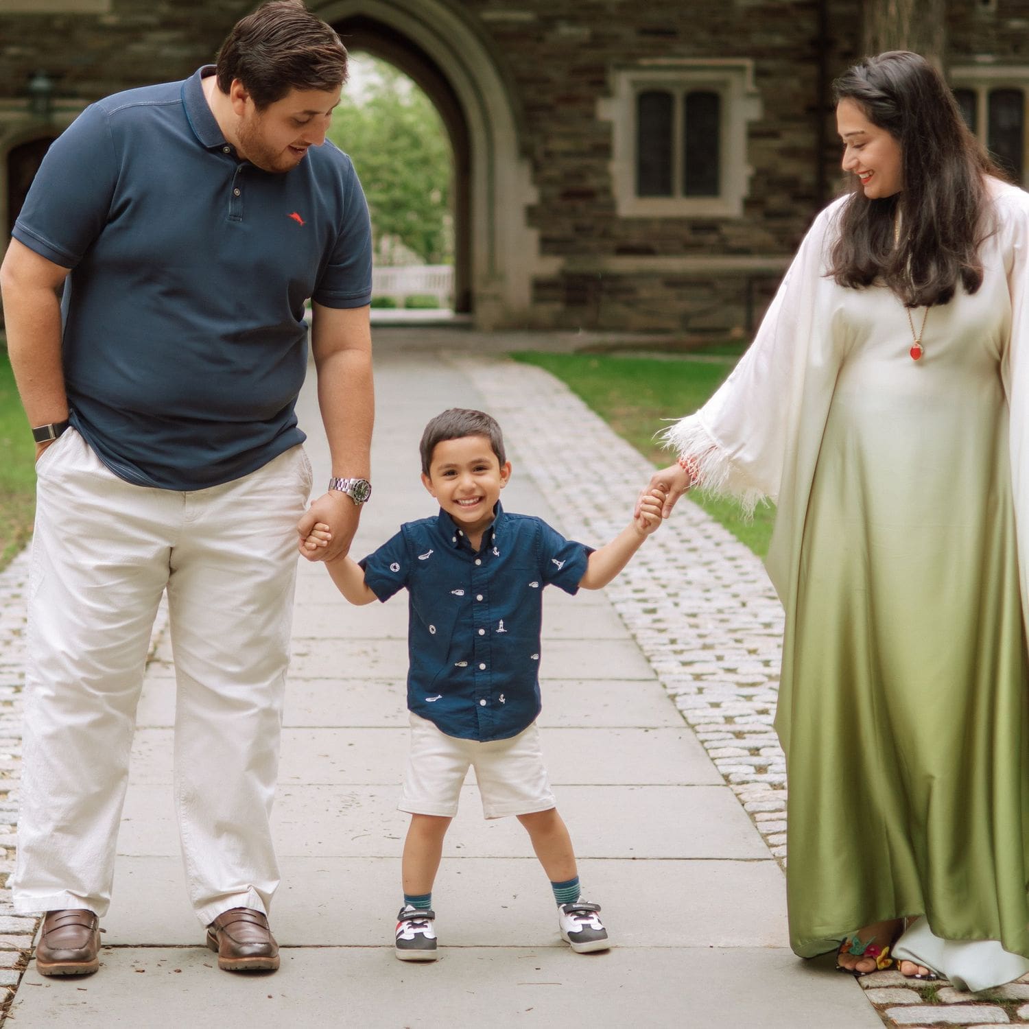 Family in coordinated outfits holding hands under a stone archway at Princeton University