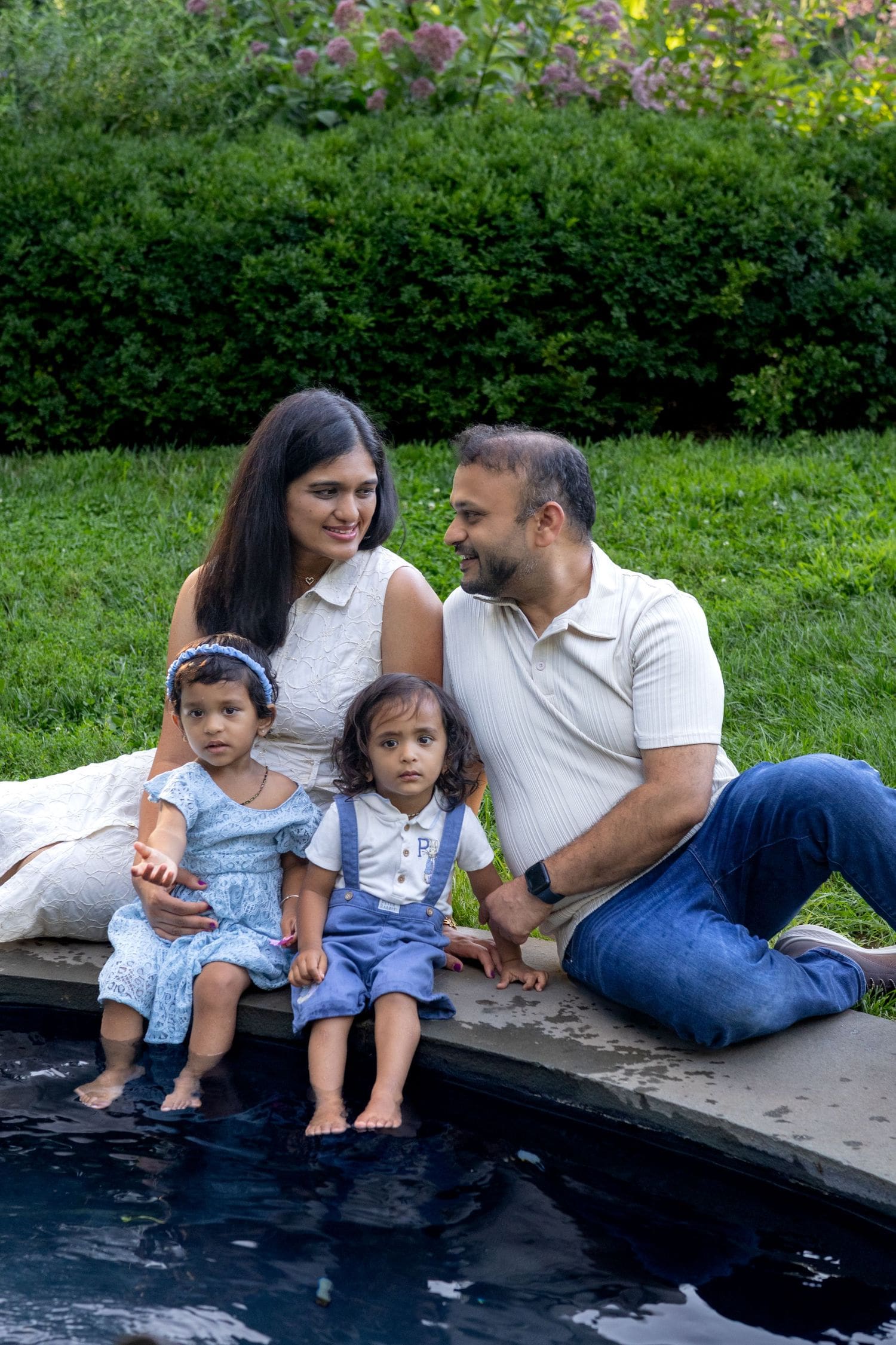 Family of four in white and denim sitting by a garden pool for an outdoor family session